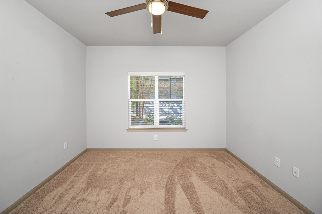 A room with a ceiling fan and a window with a view of a parking lot.